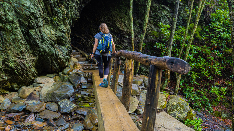 A hiker walking across a plank over a stream, towards a cave
