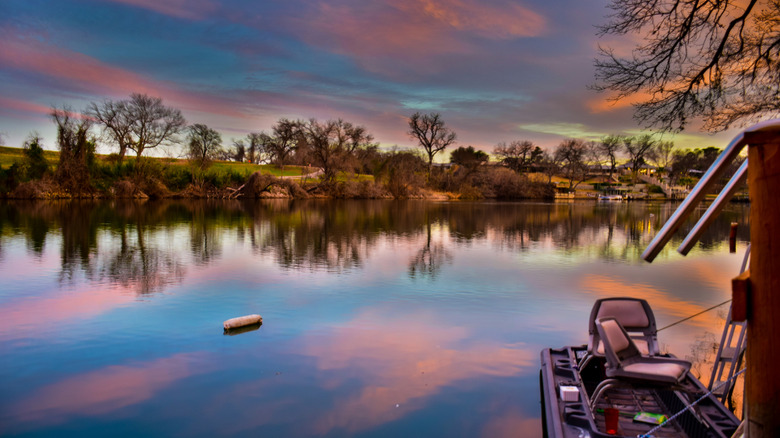 A colorful reflection of Lake LBJ at sunset with trees and lakeside homes in the distance.