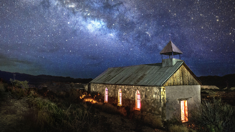 an old church illuminated at night with milky way above