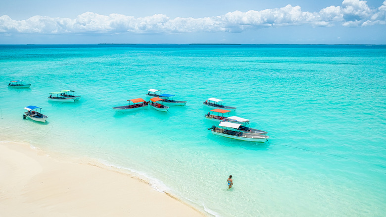 Aerial view of a group of boats anchored near a tropical beach with white sand and turquoise water in Pungume Island SandBank, Kizimkazi, Zanzibar, Tanzania, Africa, with a tourist walking in the shallow water