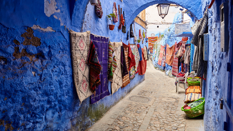 Handmade Moroccan rugs hanging from the blue walls of an alleway in Chefchaouen