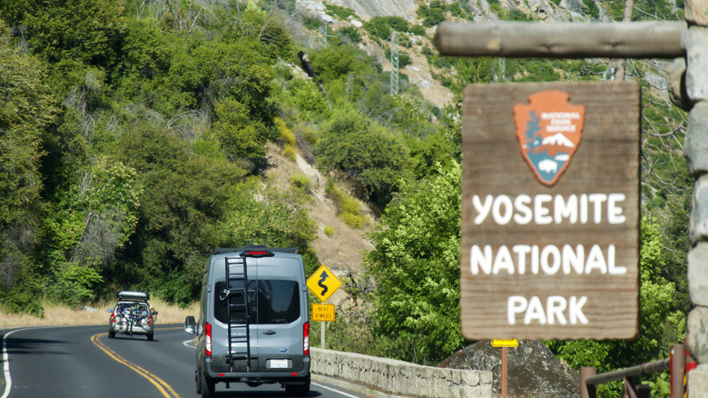 Vehicles enter Yosemite National Park at the El Portal entrance after passing by a wooden sign welcoming them to the popular destination in Northern California.
