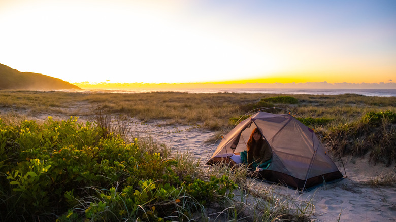 Woman smiling in a tent set up on the sand and grass near the Australian coast