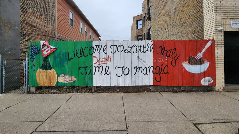 View of Chicago sidewalk with "Welcome to Little Italy. Time to Mangia." sign painted on fence with Italian flag, red, white and green