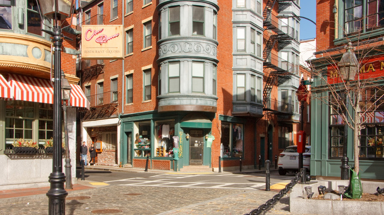 View of Little Italy neighborhood in Boston's North End with striped restaurant awnings, brick facades, and Italian restaurant signs like "Ciao Roma"