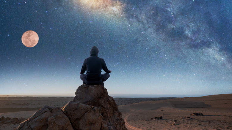 Person sitting cross-legged on a rock overlooking the Atacama Desert under a starry sky