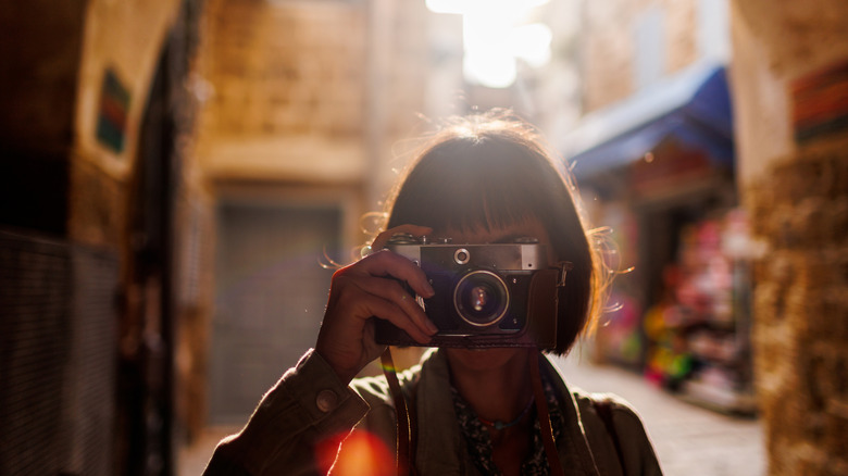 Short-haired woman taking a picture with an analog camera in a sandstone passageway