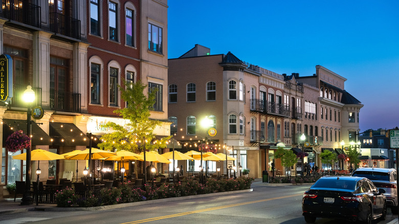 A street in downtown Carmel at dusk, with restaurant terrace seating, buildings, and parked cars