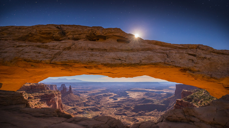 moon rising over an arch rock formation with a view of a deep canyon below