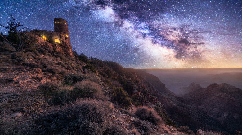 view of the milky way overlooking a canyon and a small stone house in the foreground