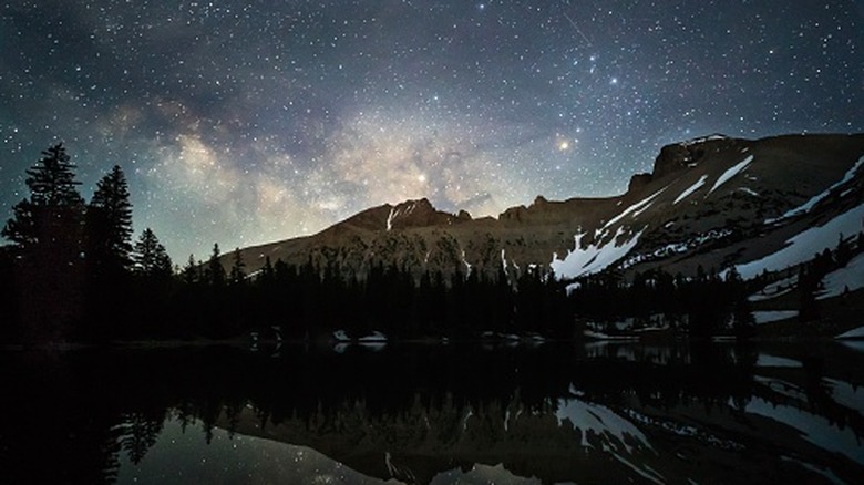 stars reflecting in late with snow covered mountain at night starry sky above