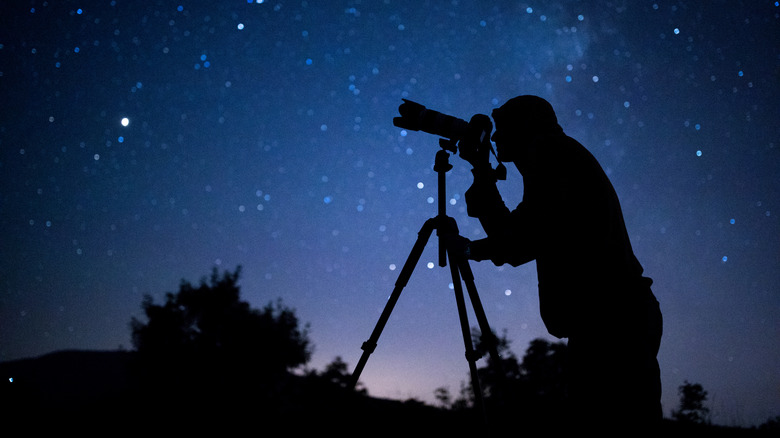 photographer gazing through camera under starry sky at night