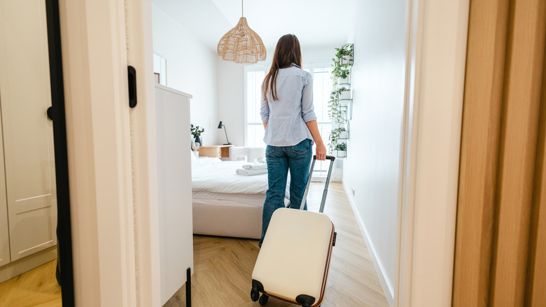 Rear view of a woman entering a hotel room with her suitcase