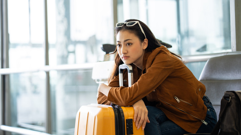 An unhappy or concerned young Asian woman with her luggage