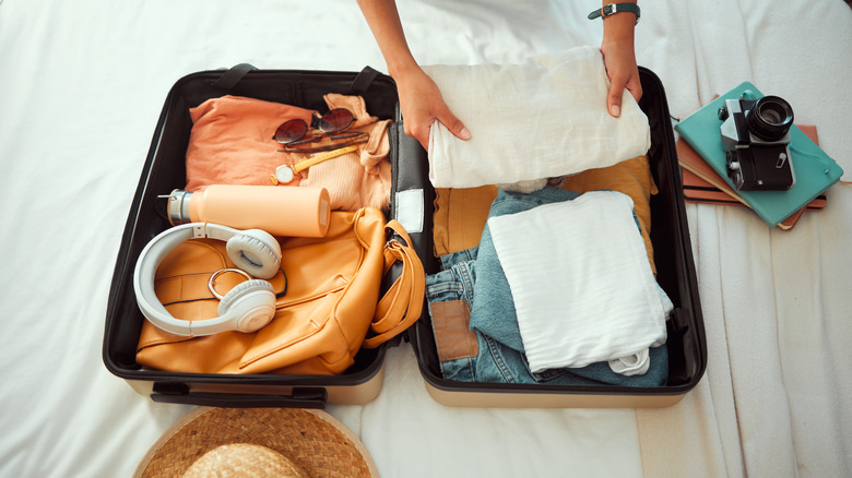 A person packs a small suitcase with clothes and other belongings