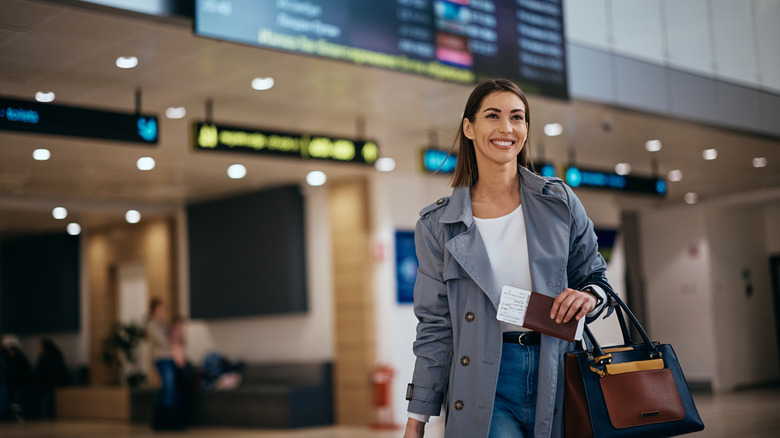 Smiling traveler in an airport holding a passport and handbag