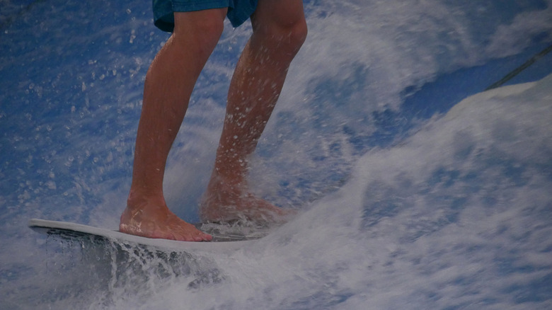 Front view of a surf rider's feet planted firmly on the surf board floating against the water flow on a FlowRider surf simulation machine