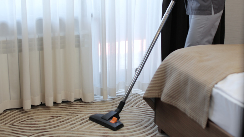 A hotel cleaner vacuuming a room