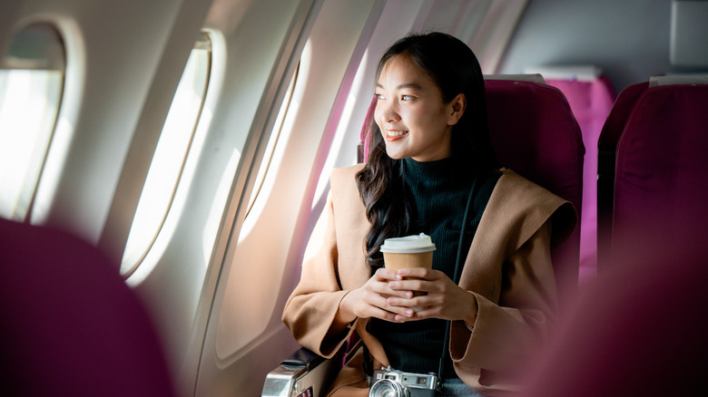 traveler smiles while holding a coffee cup looking out airplane window