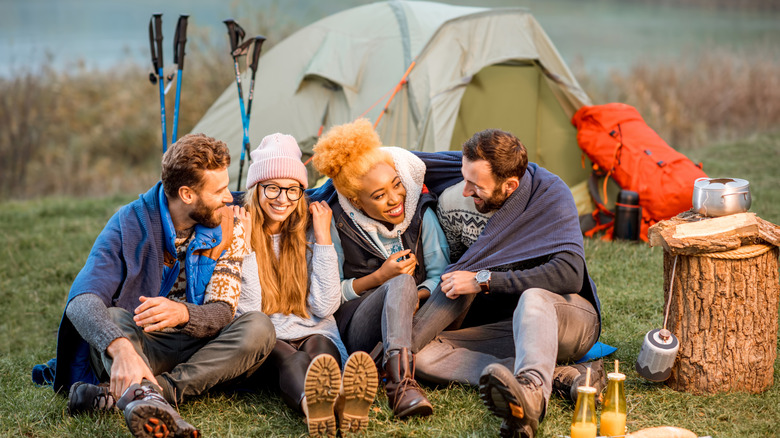 Friends on a camping trip sitting in front of a tent, laughing.