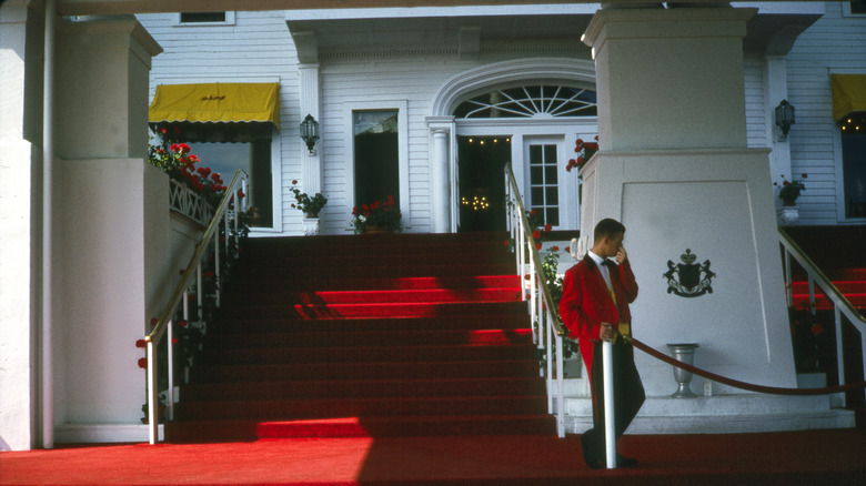 A uniformed worker stands on a red carpet next to a velvet rope at Mackinaw Island's Grand Hotel