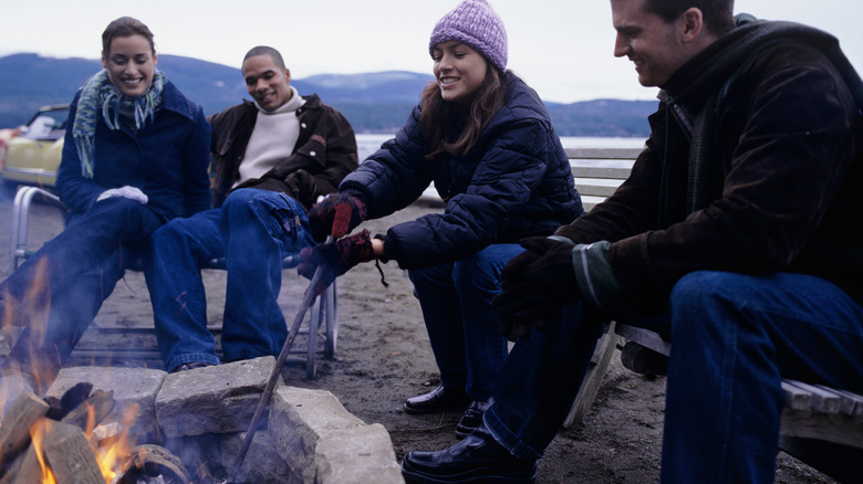 People sitting around a campfire, wearing jackets, hats, and scarves