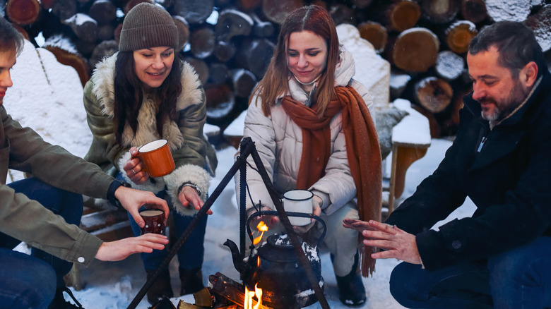 Campers drinking hot beverages around a fire