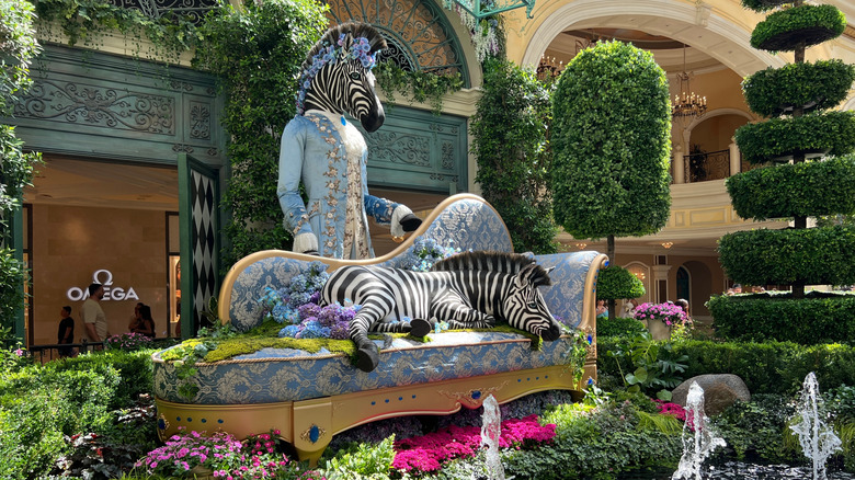 A zebra statue laying on a sofa surrounded by flowers and moss
