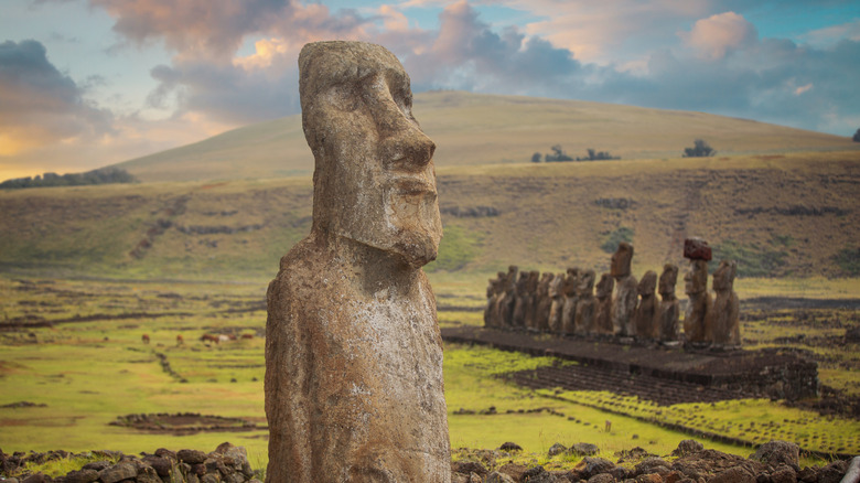 Moai statue standing alone in front of a row of statues on the green landscape of Easter Island, Chile