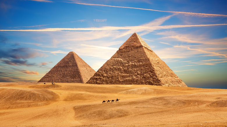 Small figures of camels in front of giant Pyramids of Giza in the Egyptian desert