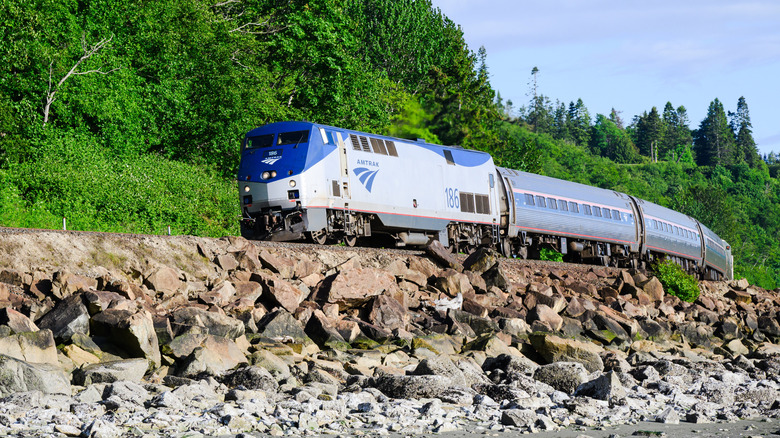 an amtrak train with rocks in foreground and trees in background