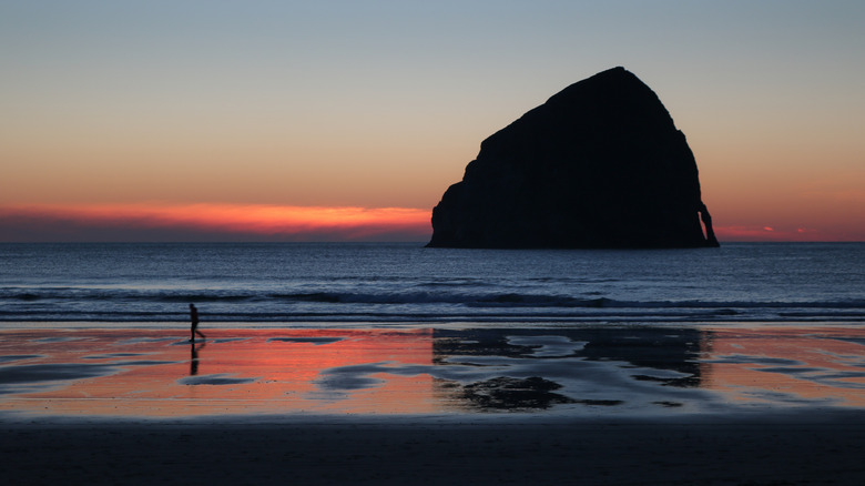 A person walks across the sand at sunset in front of Haystack Rock at Cape Kiwanda, near Pacific City, Oregon