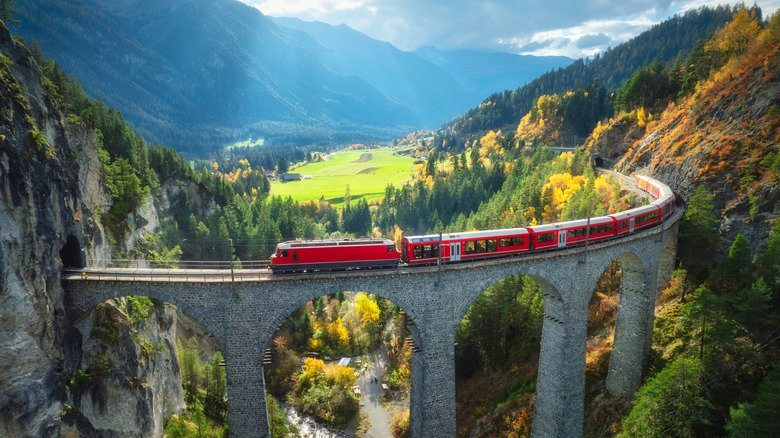 Red train of the Bernina Express crossing a viaduct in the Swiss Alps near a green valley