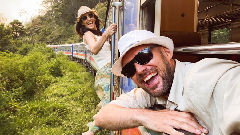 Happy tourists in sunglasses hang out of a scenic train in Sri Lanka
