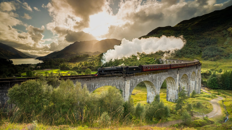 Steam train on the stone Glenfinnan Viaduct in the Scottish Highlands near a lake and green scenery