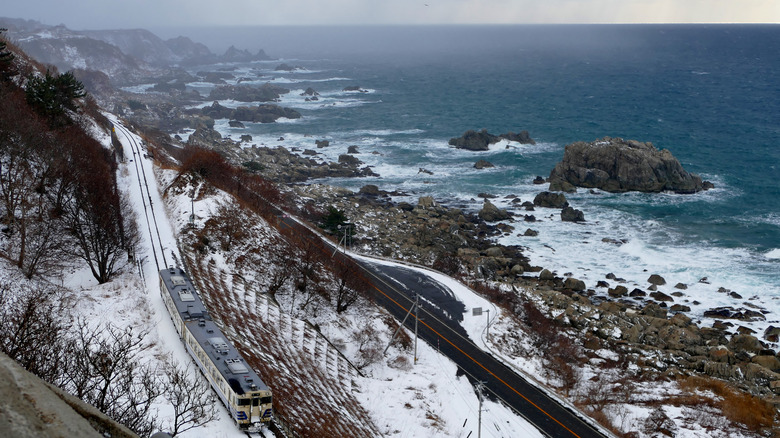 Aerial view of a white train traveling near the coast of Japan on a snowy winter's day