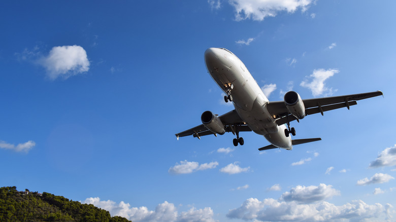 Commercial plane in flight on a partially clear day with green hill in background