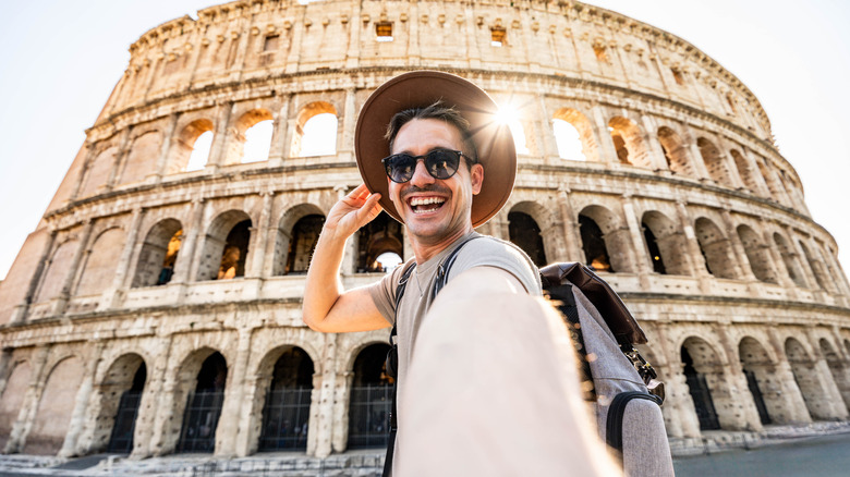 A smiling male tourist takes a selfie in front of the Roman colosseum