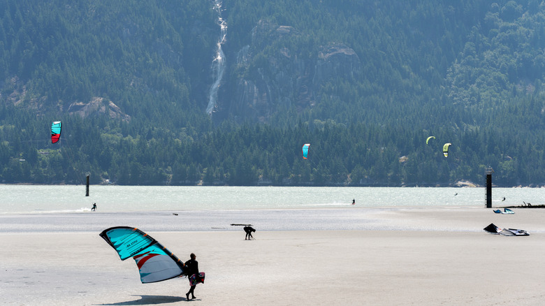 Kite and wind surfers dot the surface of the water with a waterfall cascading down in the background