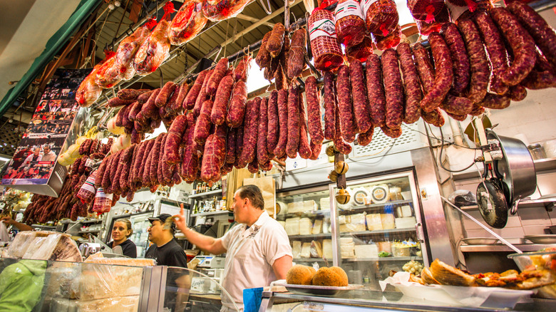 A man works behind the counter under hanging sausages in the Bronx's Little Italy, NYC