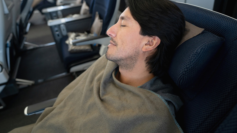 A passenger sleeping under a blanket on a plane
