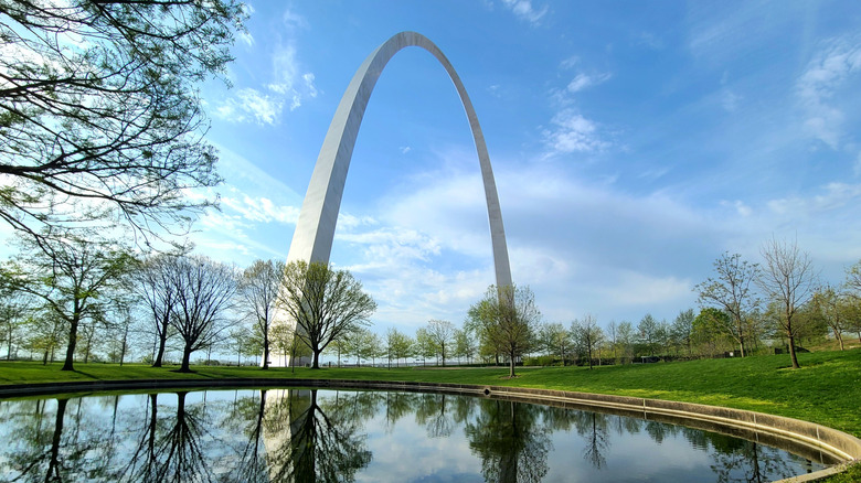 Missouri's Gateway Arch monument reflected in a nearby pool by a grassy field