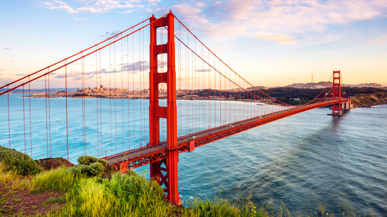 Golden Gate Bridge crossing the opaque blue water of the San Francisco Bay on a sunny day at sunset with the city behind it