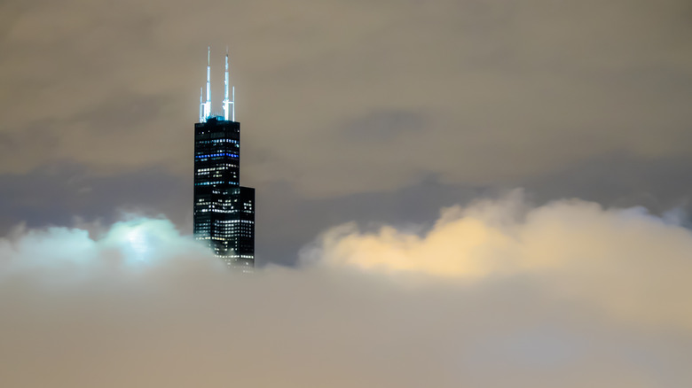 Chicago's black Willis Tower (formerly Sears) is lit up, tall above clouds on a rainy night