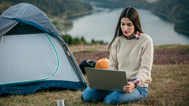 woman using her laptop near camping tent in the forest