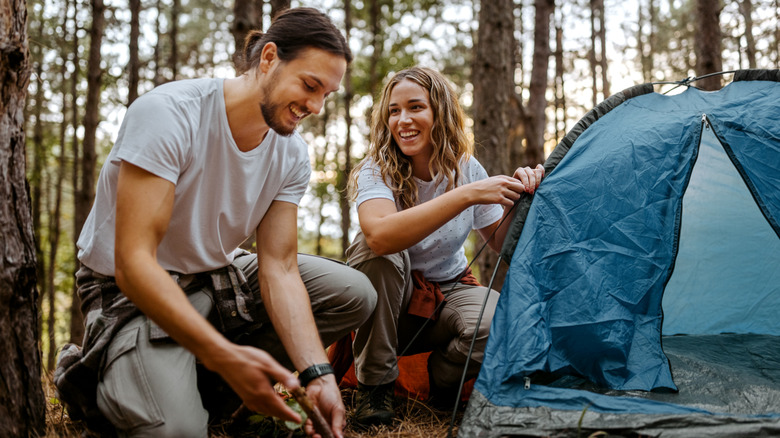 smiling woman and man setting up camp tent