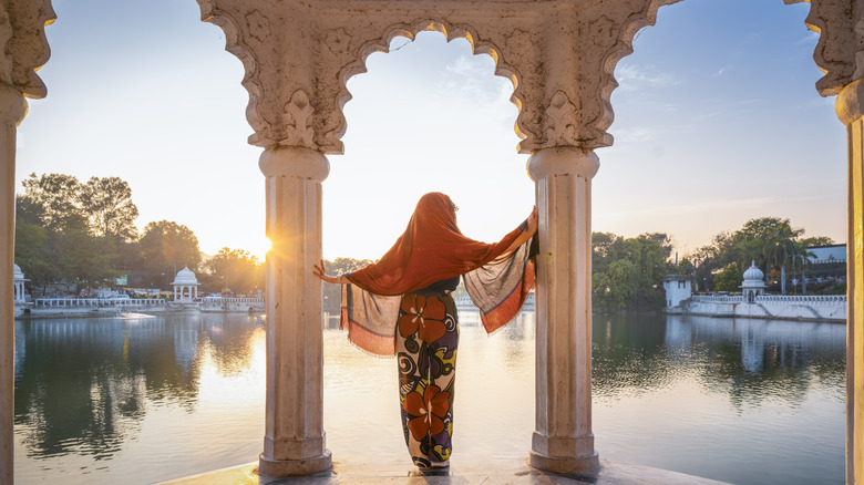 A woman wearing a head covering looking out over the water from an archway in India