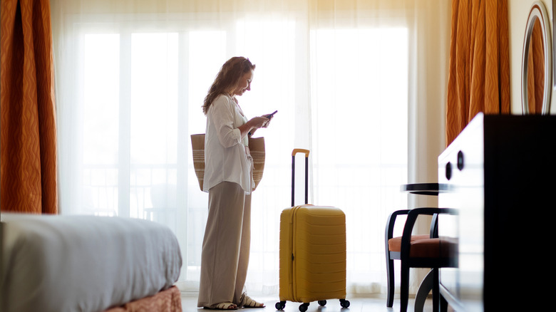 A woman standing in hotel room looking at her phone.