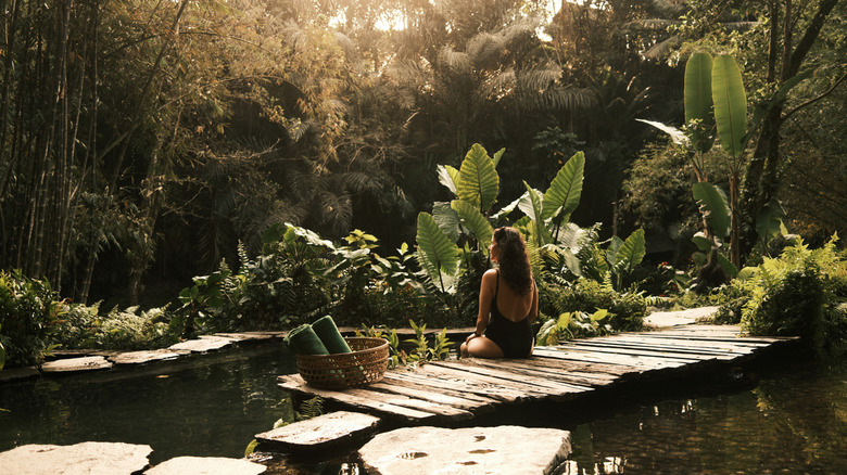 Woman sitting on a wooden pier alone in a sunny jungle forest on the water