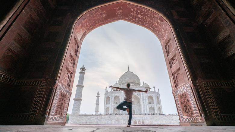 Man doing a yoga pose in front of India's Taj Mahal framed by a ornate doorway